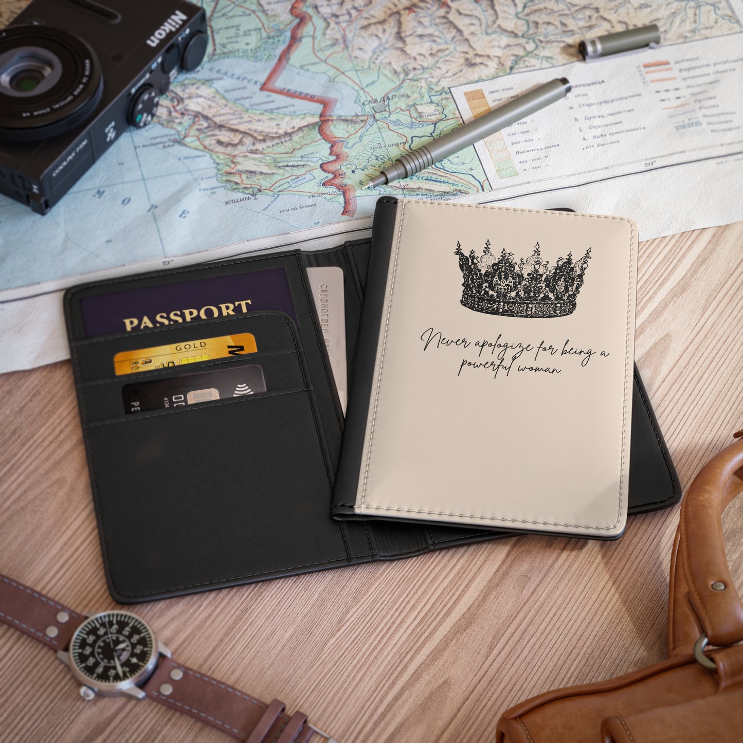 A perspective image with the passport book opened and close. It is on a desk with a map, watch, camera  and handles of a small tote bag